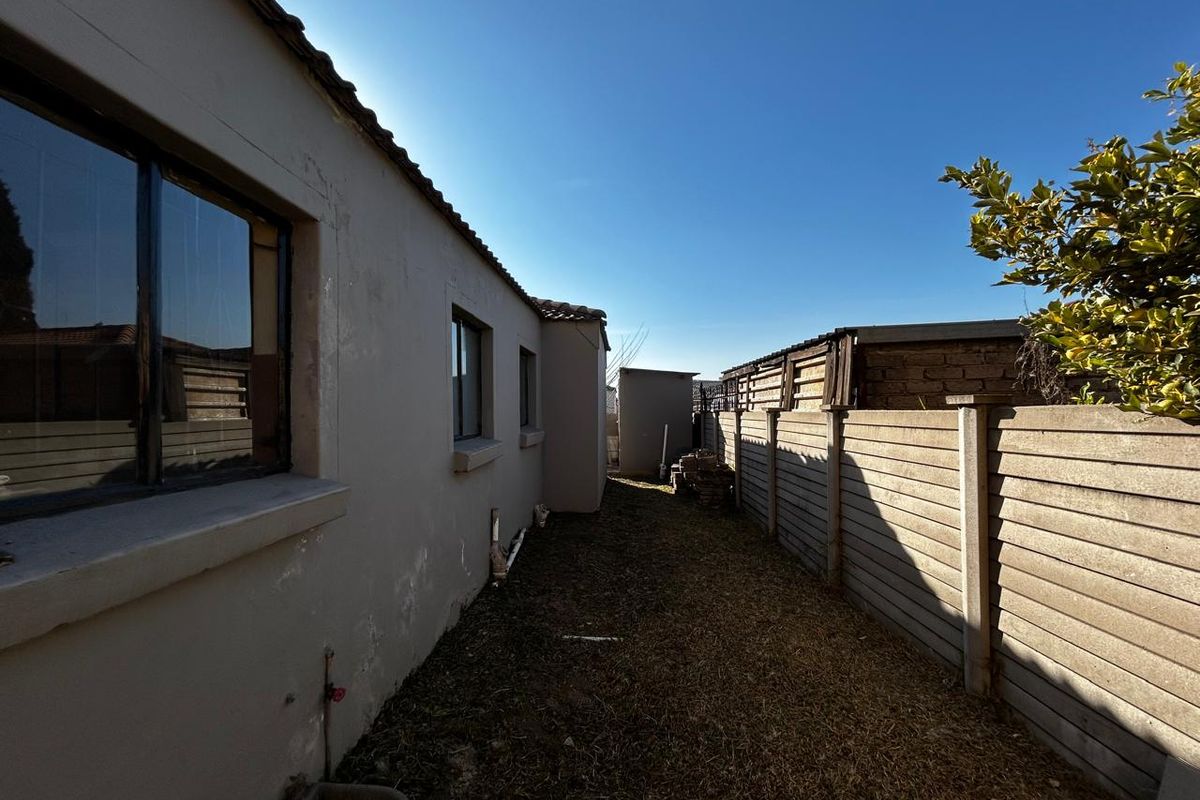 A view of the rear exterior side passage featuring a precast concrete boundary wall and basic building facade.