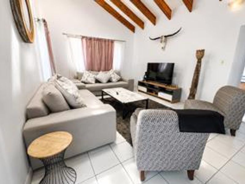 Spacious living room featuring a high vaulted ceiling with exposed timber beams and neutral tiled flooring, creating an open and airy atmosphere.