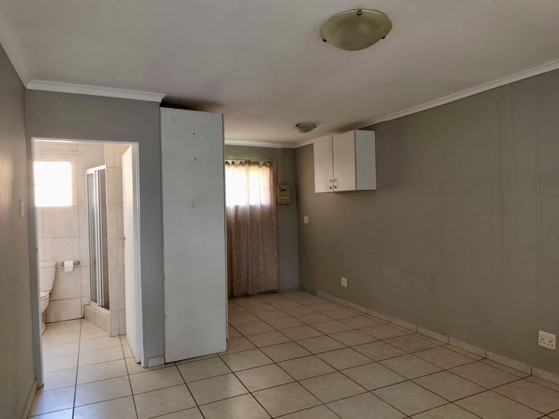 An empty bedroom featuring tiled flooring, neutral wall paint, and an attached en-suite bathroom, offering a blank canvas for renovation or interior design updates.