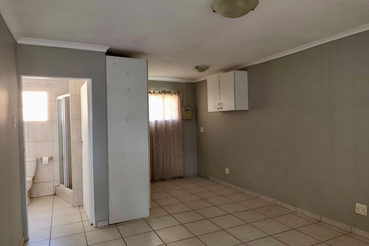 An empty bedroom featuring tiled flooring, neutral wall paint, and an attached en-suite bathroom, offering a blank canvas for renovation or interior design updates.