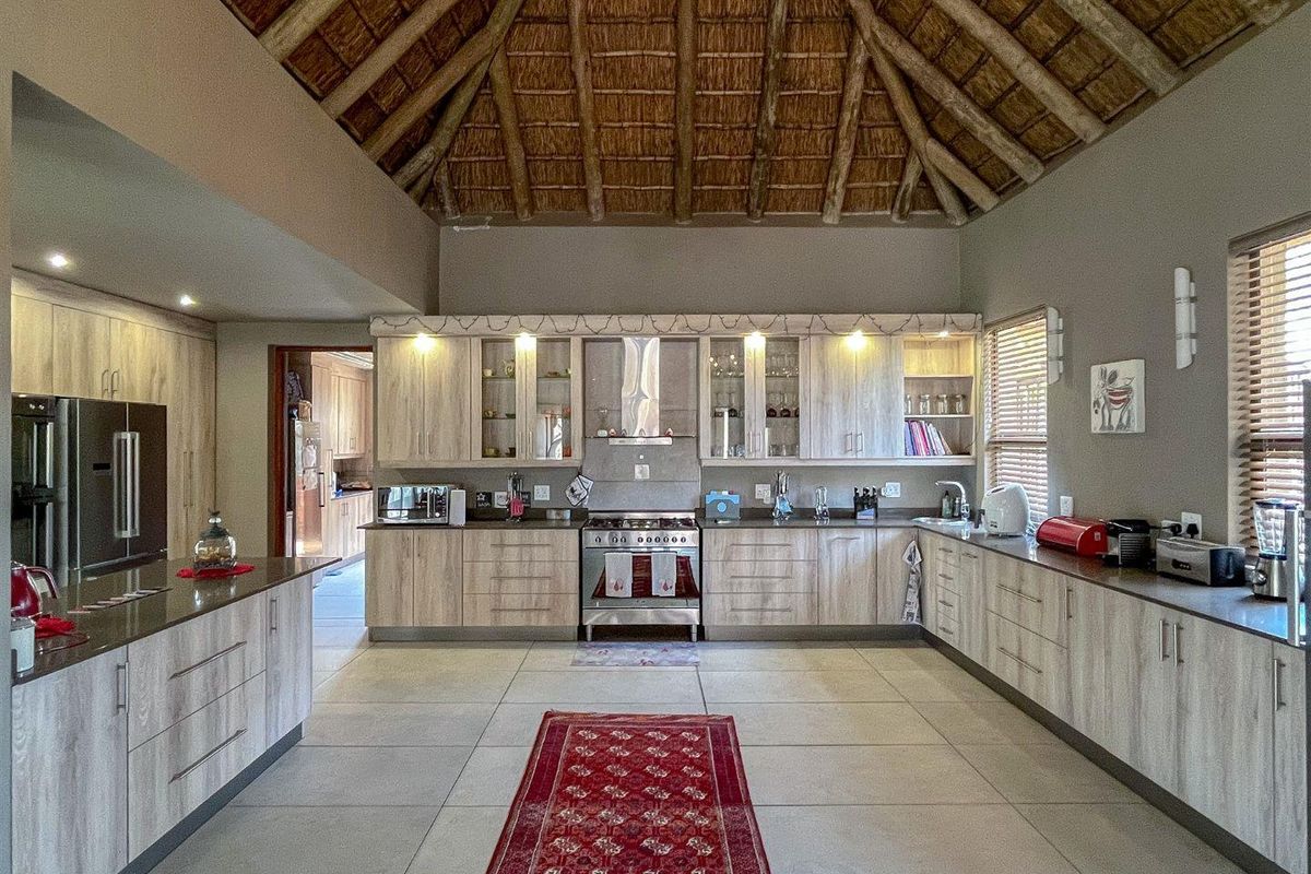 Spacious kitchen featuring light wood cabinetry, granite countertops, a gas stove with extractor fan, and a distinctive high-pitched thatched ceiling.