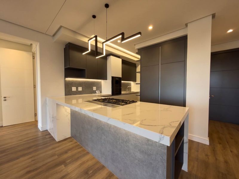 Modern kitchen featuring a marble-look stone island with integrated gas hob, sleek dark cabinetry, and contemporary pendant lighting in an open-plan layout.