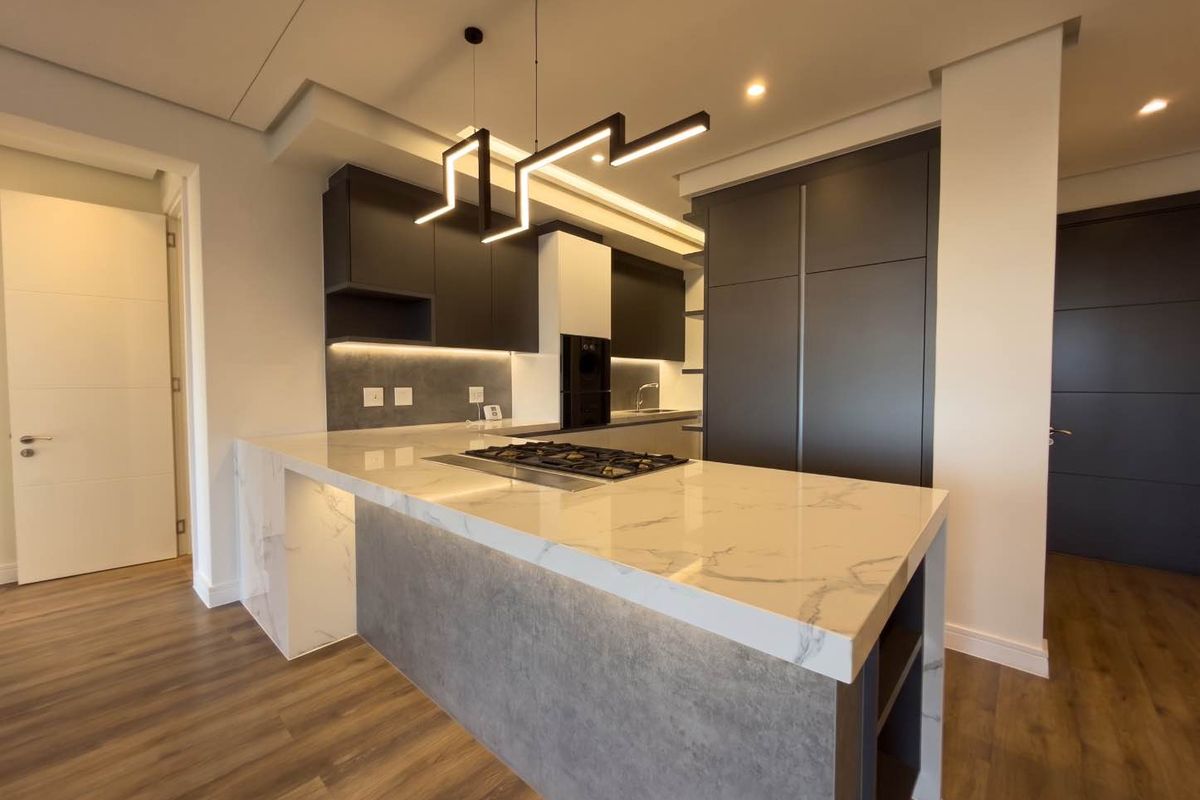 Modern kitchen featuring a marble-look stone island with integrated gas hob, sleek dark cabinetry, and contemporary pendant lighting in an open-plan layout.