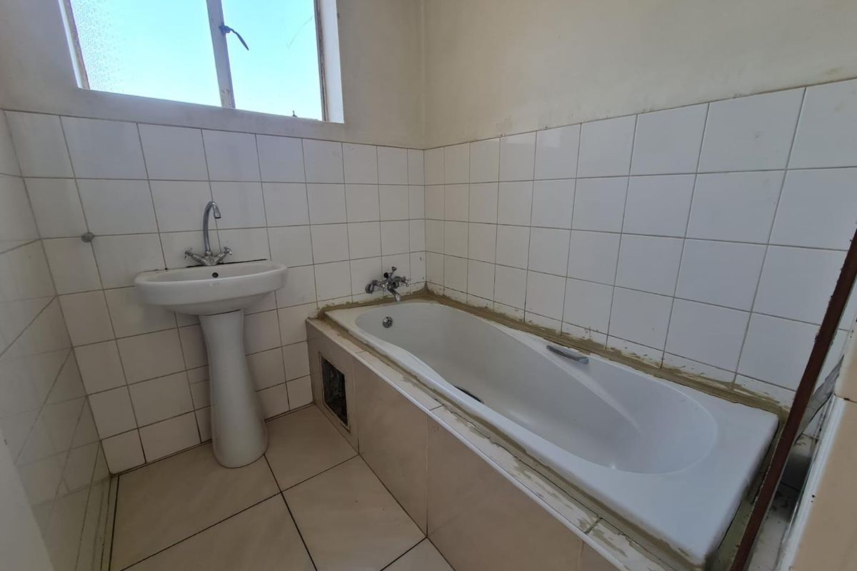 A functional bathroom featuring a pedestal basin and a built-in bathtub with tiled surround, requiring minor finishing touches to the tiling and sealant.