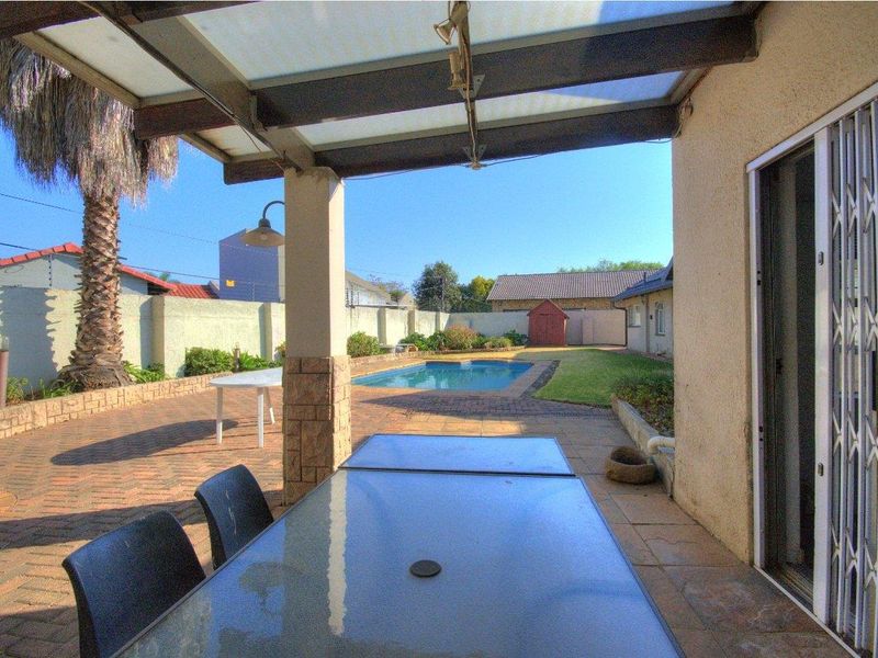 Covered patio area overlooking a private swimming pool and garden, featuring brick paving and direct access to the main house.