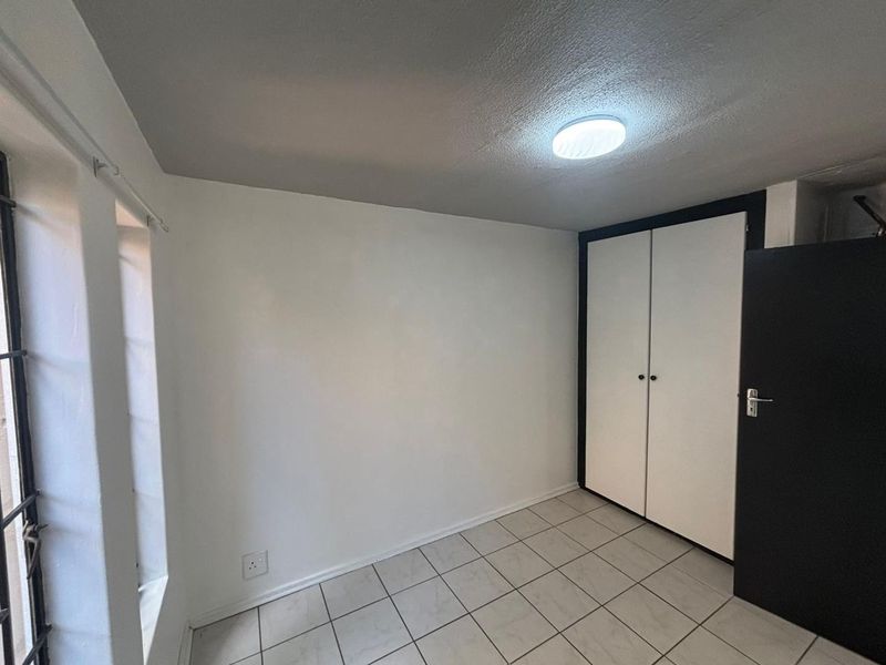 A clean, empty bedroom featuring tiled flooring, built-in cupboards, and a secure window with security bars.