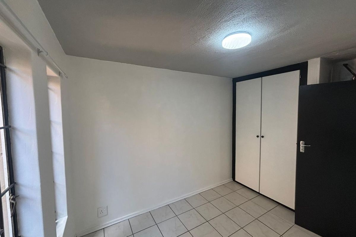 A clean, empty bedroom featuring tiled flooring, built-in cupboards, and a secure window with security bars.