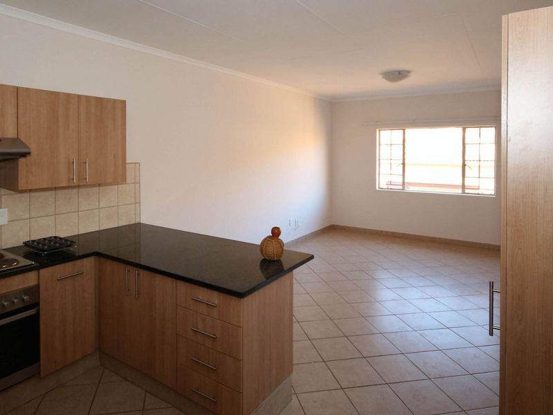 An open-plan kitchen and living area featuring light wood cabinetry, granite countertops, built-in appliances, and neutral tiled flooring throughout.
