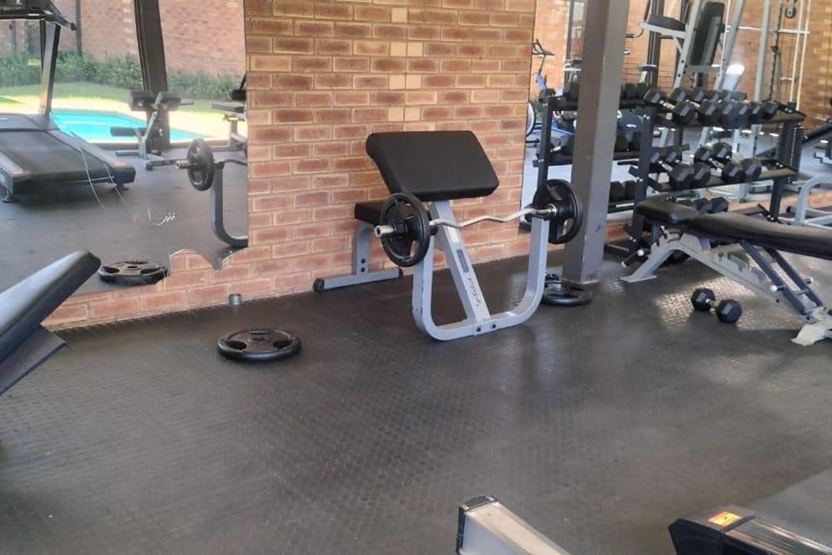 A functional home gym featuring durable rubber flooring, exposed brick wall accents, and a large wall mirror, providing a dedicated space for fitness activities.