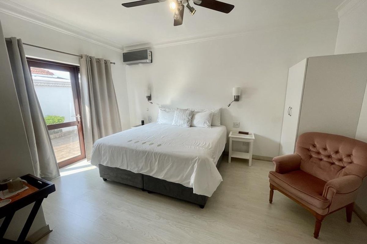 A well-maintained bedroom featuring light wood-look flooring, a ceiling fan, wall-mounted air conditioning unit, and direct access to an outdoor patio area.