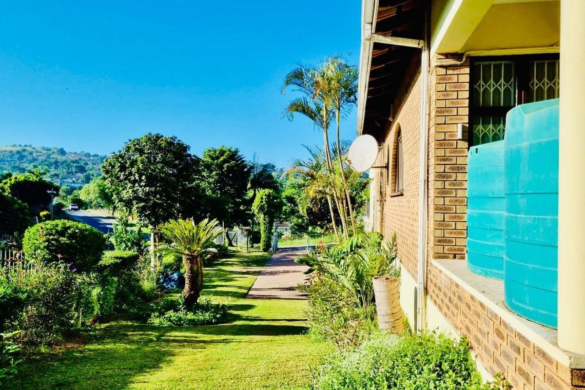 A view of the rear garden featuring a brick facade, paved walkway, and installed water storage tanks alongside established landscaping.