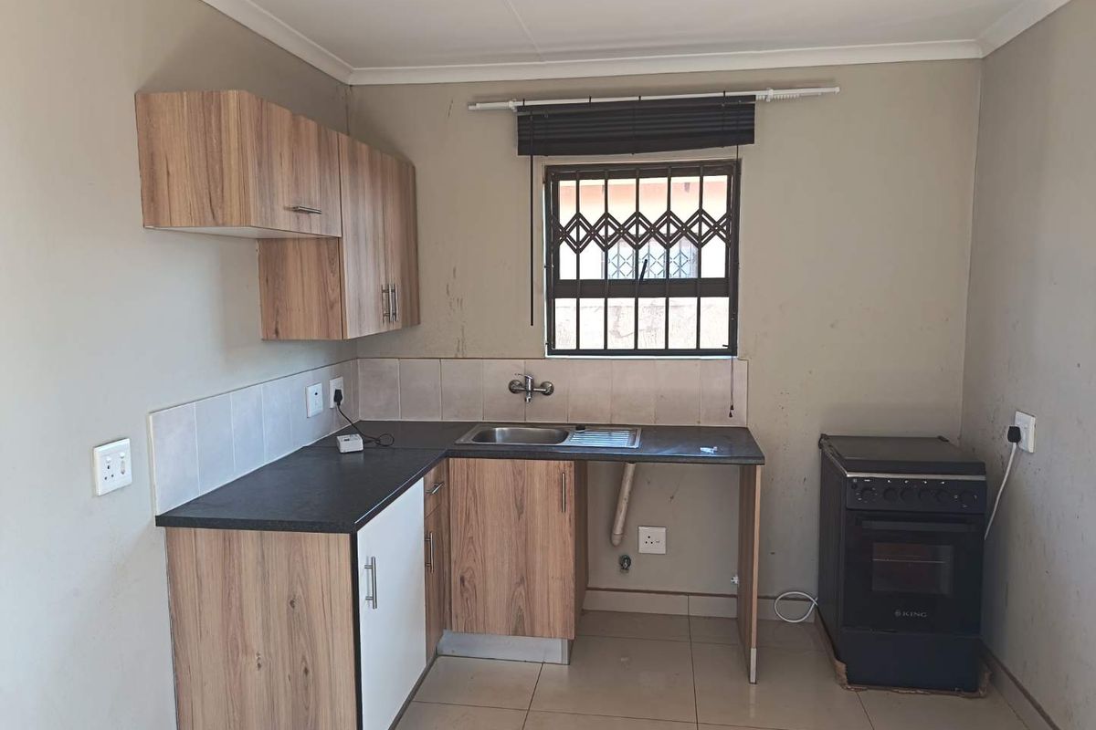 A functional kitchen featuring laminate cabinetry, dark countertops, a stainless steel sink, and a freestanding oven, with tiled flooring and security window bars.