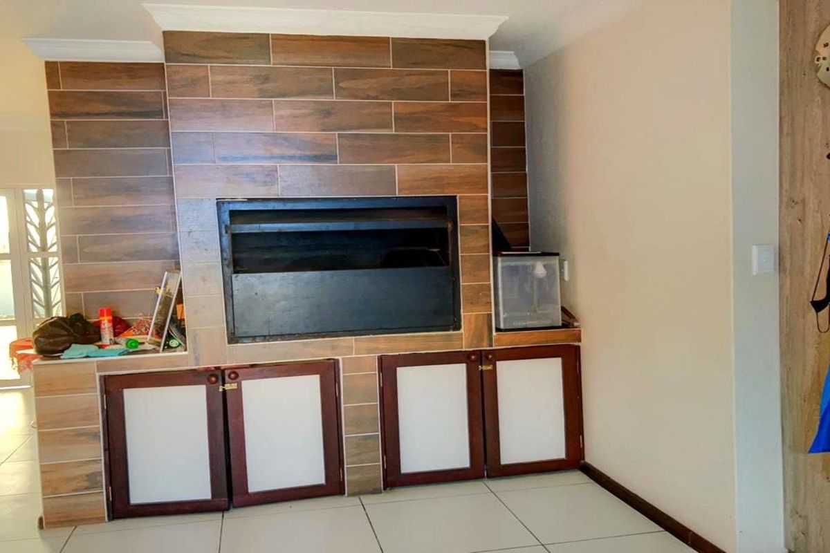 Living area featuring a prominent built-in braai with wood-look tile surround and integrated storage cabinetry.