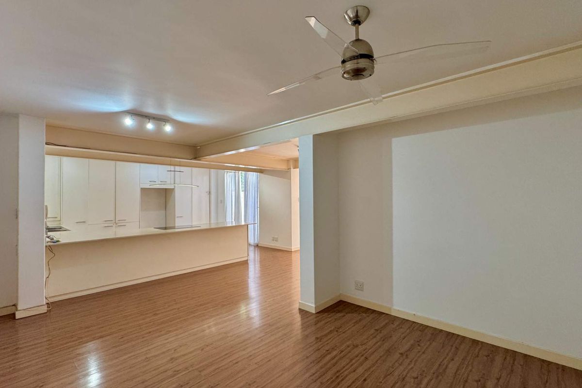 Spacious open-plan living and kitchen area featuring laminate flooring, a ceiling fan, and modern built-in cabinetry with a functional kitchen island.