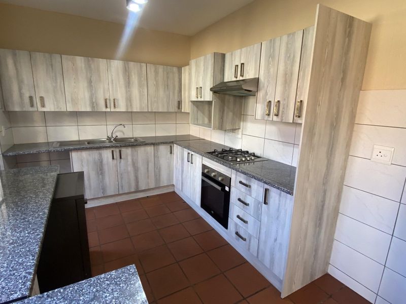 A functional kitchen featuring light wood-look cabinetry, granite countertops, a built-in oven with gas hob, and durable terracotta floor tiles.