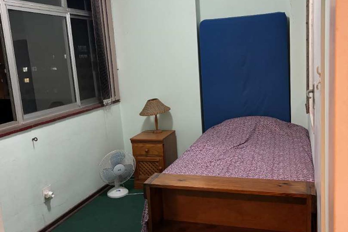 A compact bedroom featuring green carpeting, a large window with blinds, and a recessed wall alcove.