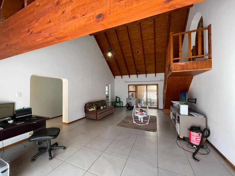 Spacious living area featuring a high vaulted timber ceiling, exposed beams, tiled flooring, and a timber staircase leading to a mezzanine level.
