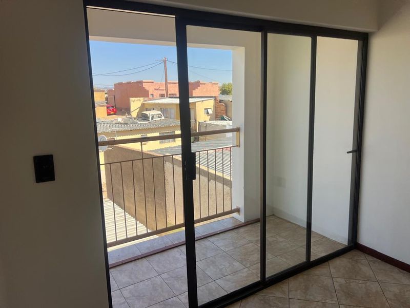 A clean, empty balcony area featuring tiled flooring, a metal balustrade, and large sliding glass doors providing access from the interior.