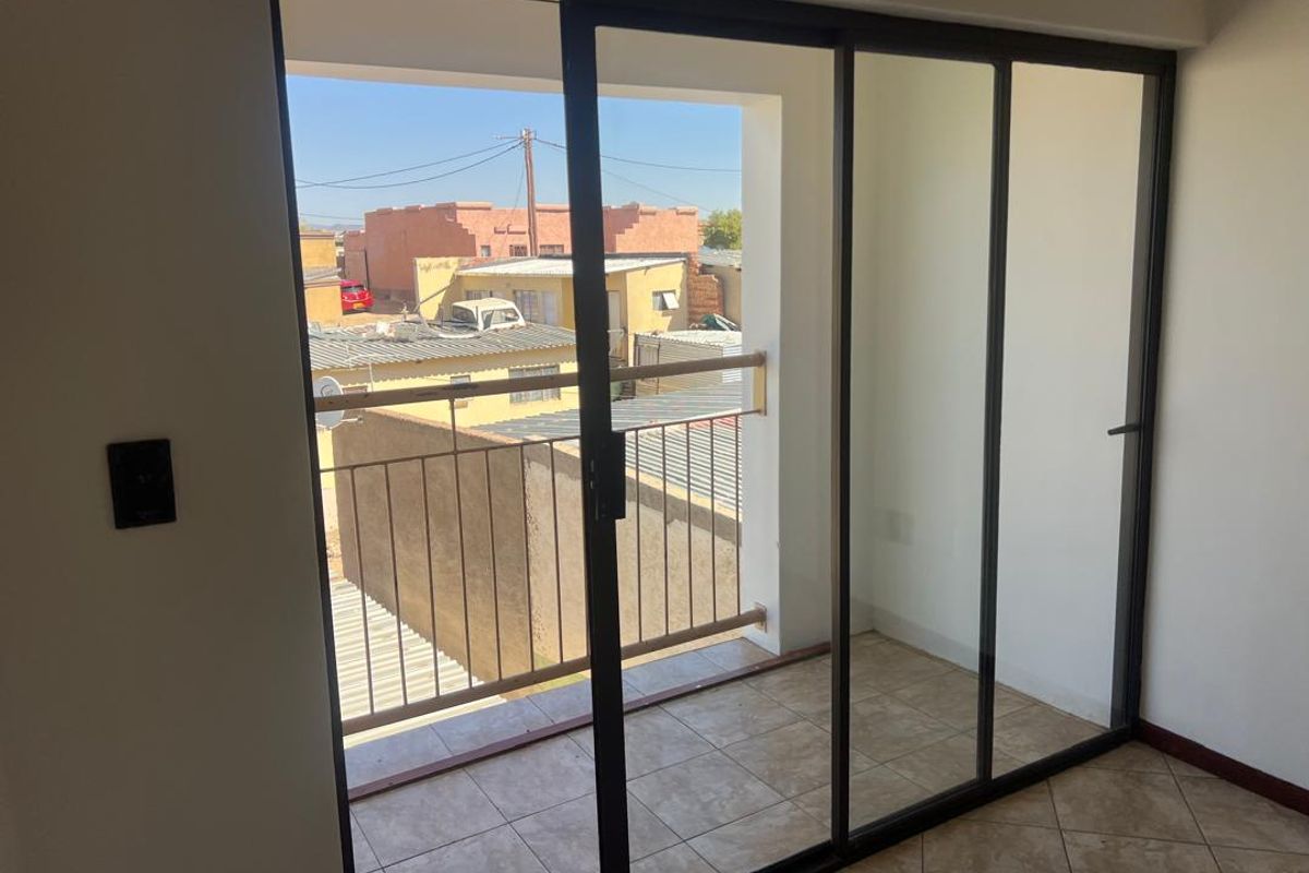 A clean, empty balcony area featuring tiled flooring, a metal balustrade, and large sliding glass doors providing access from the interior.