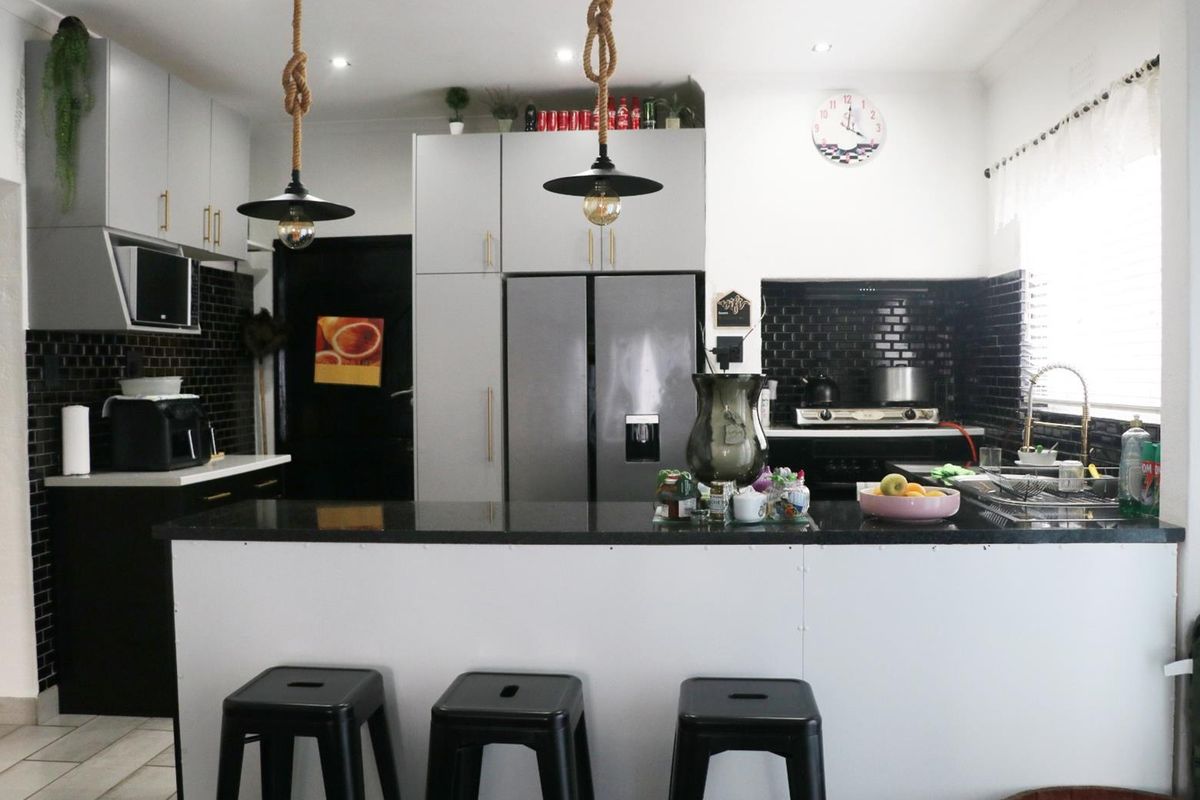 Modern kitchen featuring sleek grey cabinetry, black subway tile backsplash, stone countertops, and a functional island with breakfast bar seating.