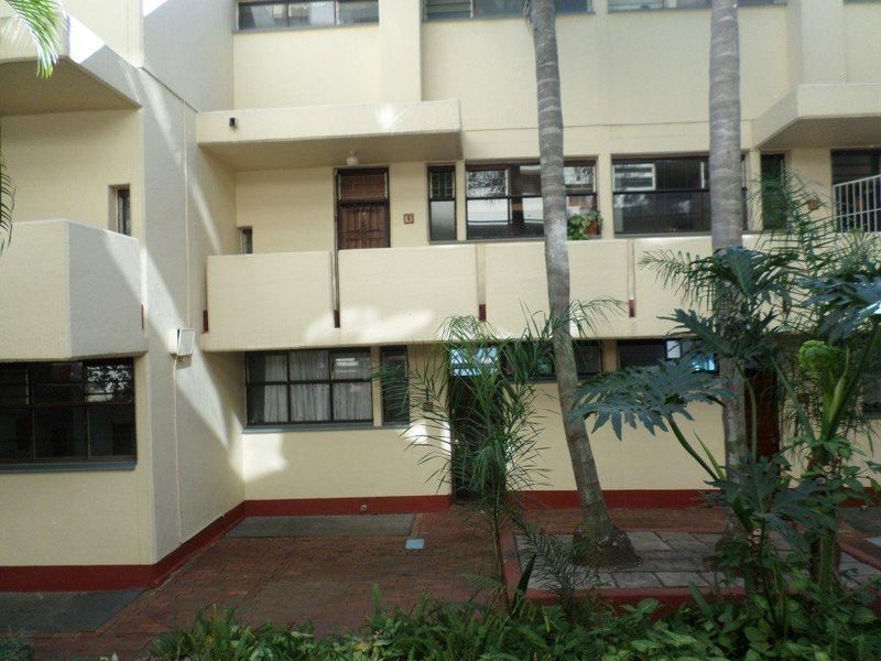 Rear view of the apartment building featuring a paved courtyard area, balconies, and established landscaping.