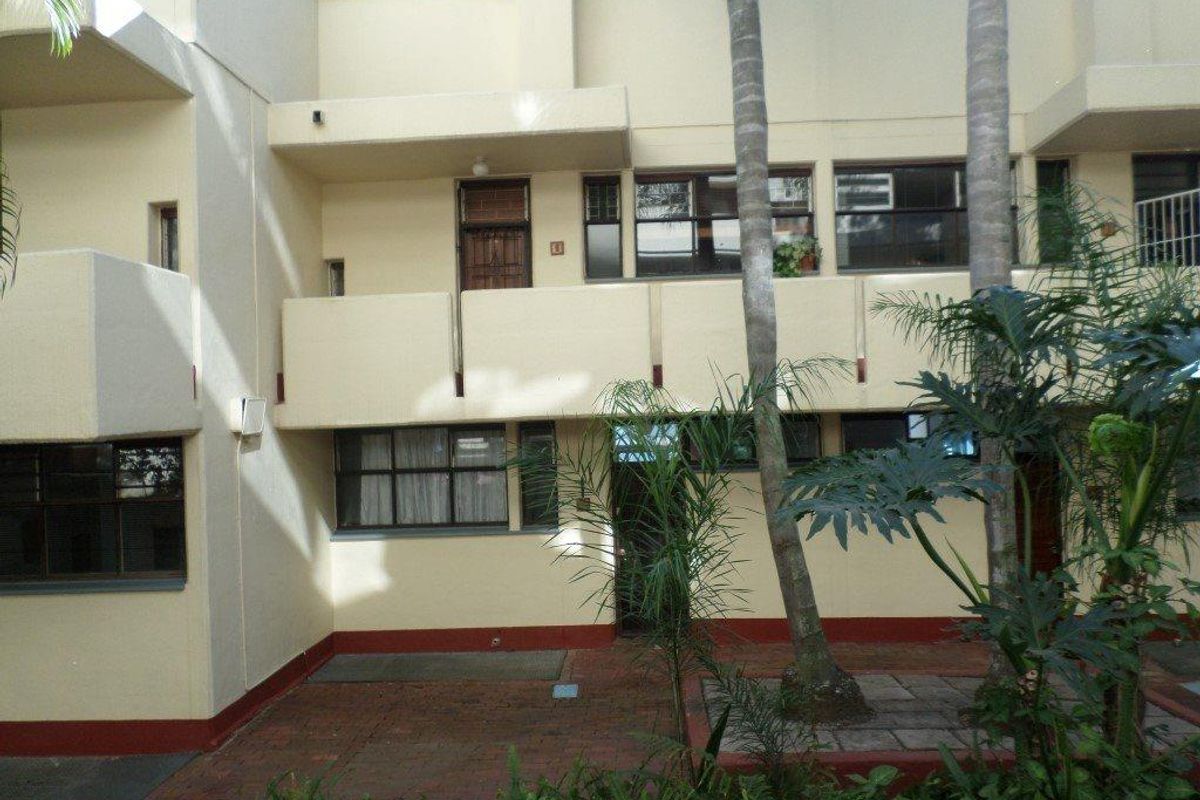 Rear view of the apartment building featuring a paved courtyard area, balconies, and established landscaping.