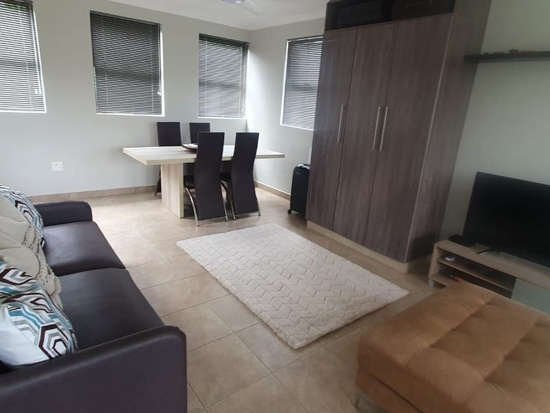 Open-plan living and dining area featuring tiled flooring, built-in storage cabinetry, and multiple windows fitted with venetian blinds.