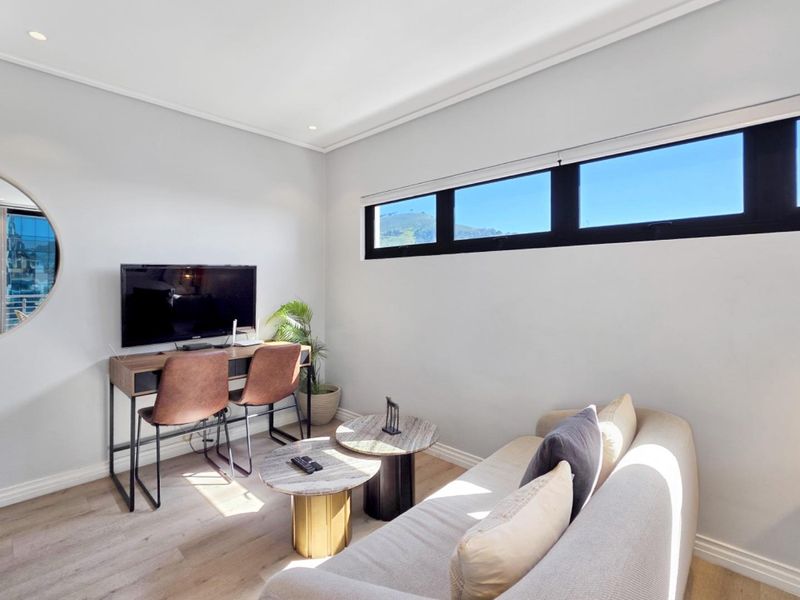 A bright and modern living area featuring light laminate flooring, recessed downlighting, and a horizontal clerestory window providing natural light.