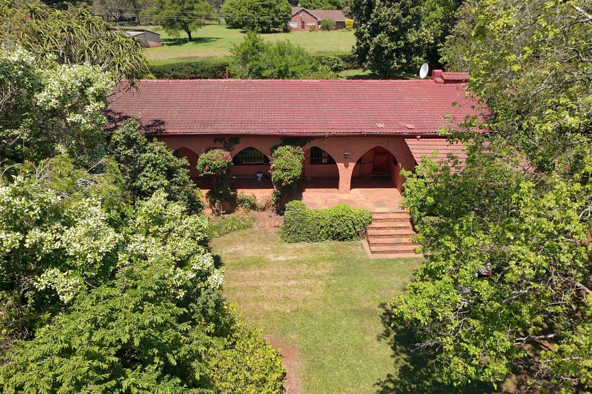 Aerial view of a single-story house featuring a tiled roof, arched veranda, and surrounding garden area.