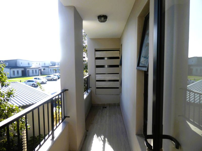 A covered balcony featuring tiled flooring, a metal balustrade, and a privacy screen, offering an elevated view of the surrounding apartment complex.