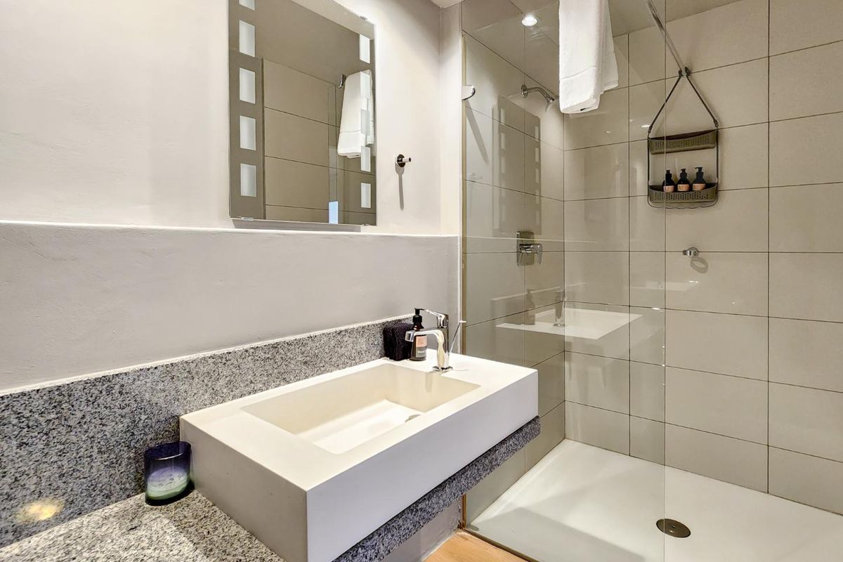 Modern bathroom featuring a granite vanity with integrated basin, chrome fixtures, and a spacious glass-enclosed walk-in shower with neutral wall tiling.