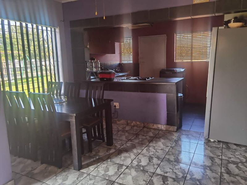 Open-plan living and kitchen area featuring tiled flooring, a central kitchen island with a built-in hob, and security bars on the windows.
