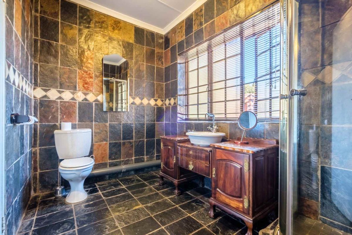 A bathroom featuring dark slate wall and floor tiles, a vessel sink vanity, a toilet, and a glass-enclosed shower.