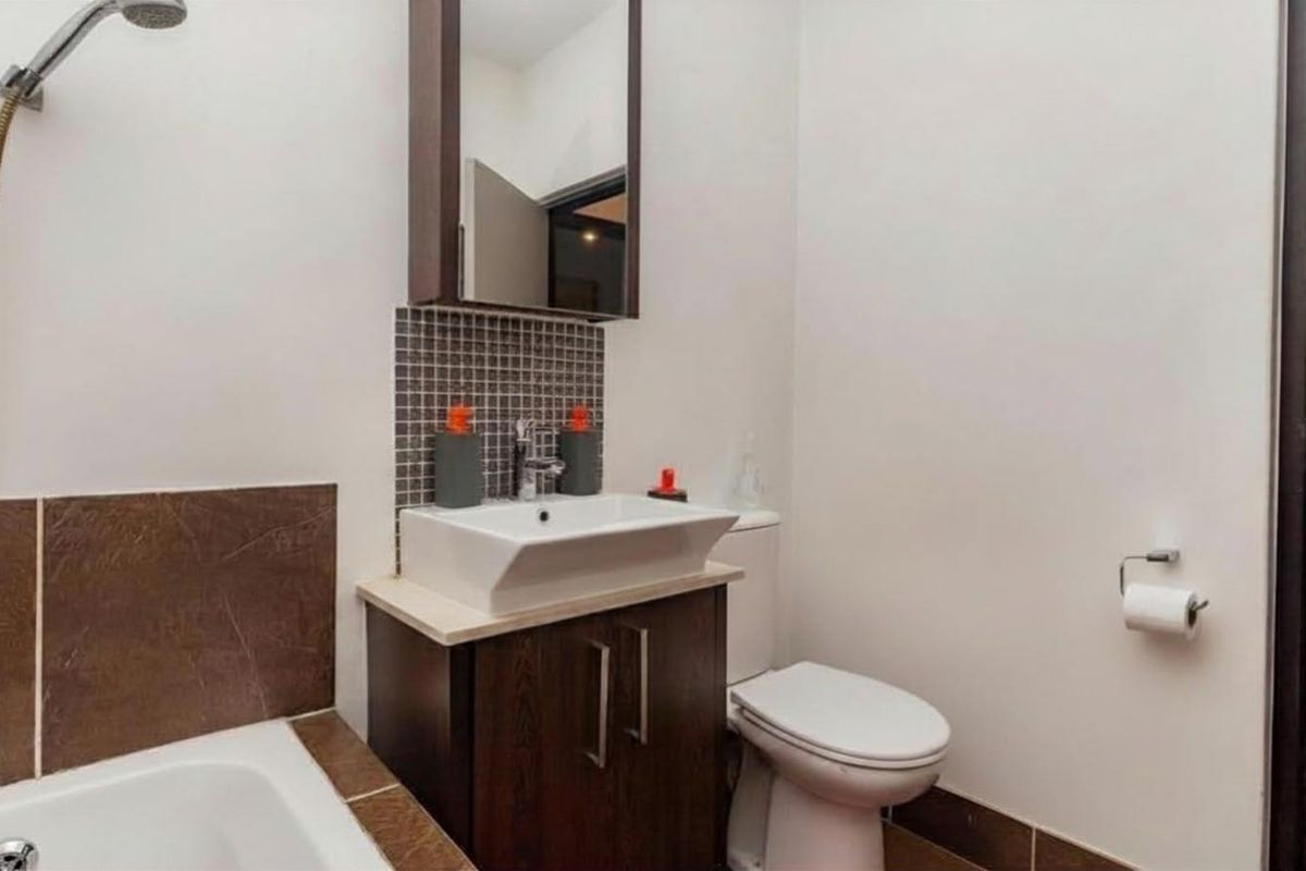 A functional bathroom featuring a bathtub with shower attachment, a modern vessel sink on a dark wood vanity, and a mirrored medicine cabinet.