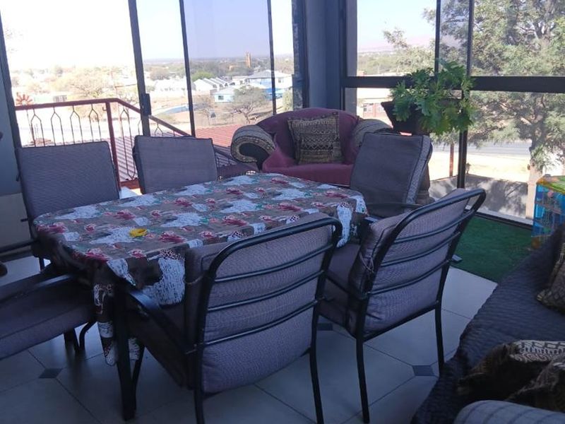 An enclosed patio area featuring tiled flooring, timber ceiling, and large glass windows providing expansive views of the surrounding neighborhood.