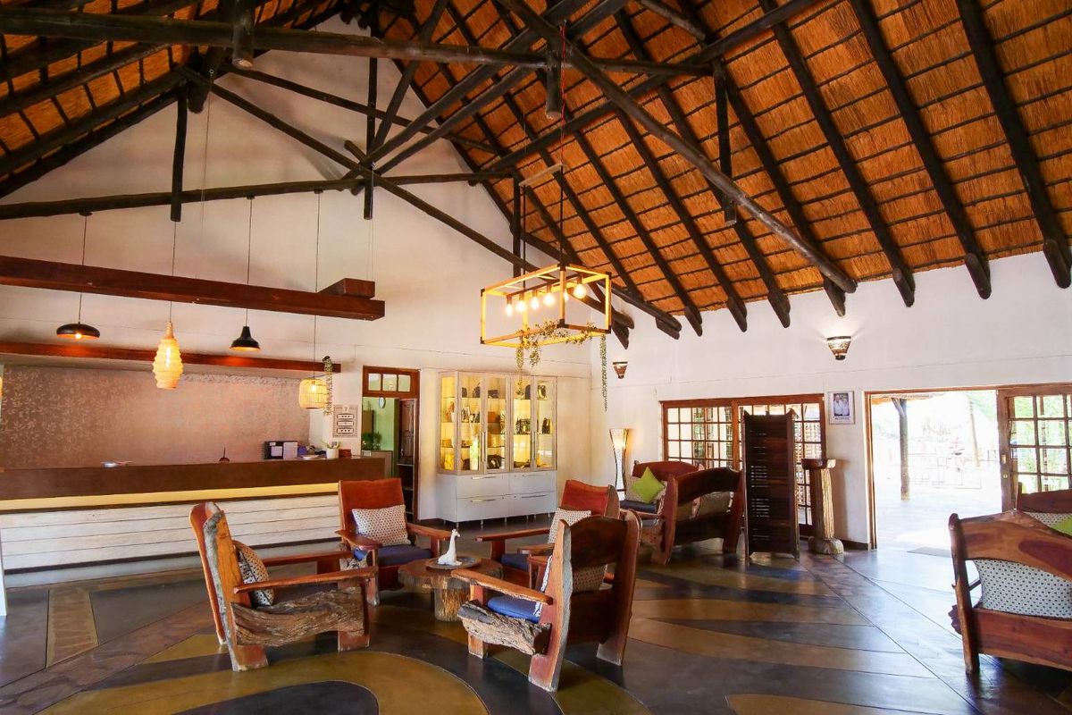 Spacious lodge reception area featuring a high vaulted thatched roof, exposed timber trusses, and polished concrete flooring with decorative inlay.