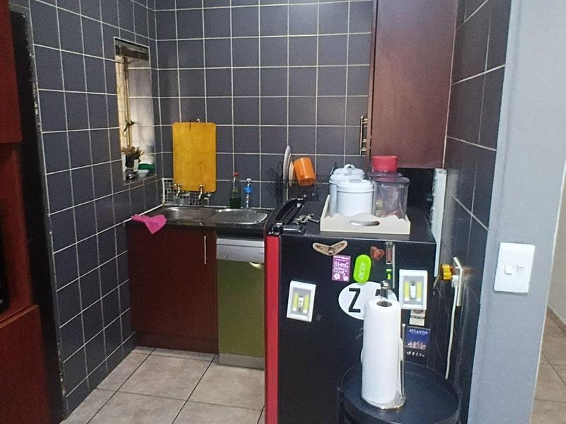A compact scullery area featuring dark tiled walls, built-in cabinetry, and a stainless steel sink, providing functional prep and wash-up space.