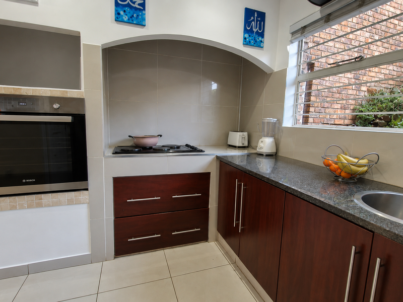 A functional kitchen featuring dark wood cabinetry, granite countertops, a built-in oven, and a hob, with a window overlooking an exterior brick wall.