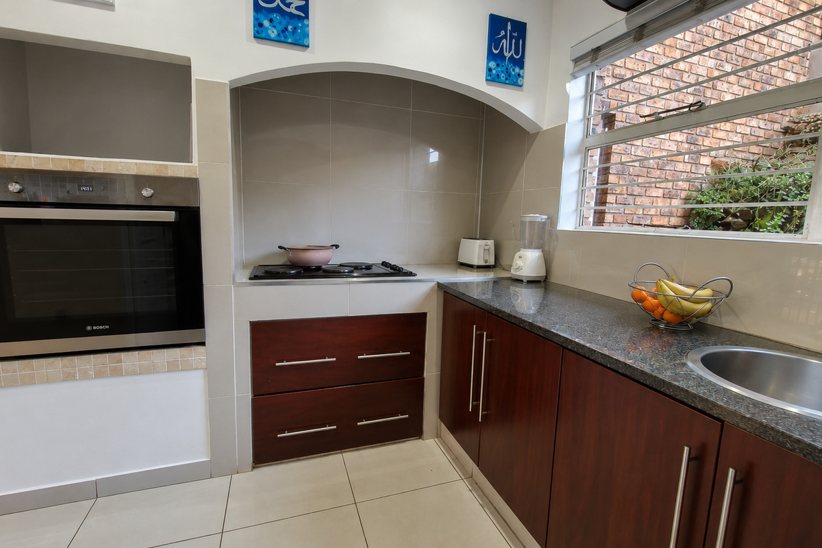 A functional kitchen featuring dark wood cabinetry, granite countertops, a built-in oven, and a hob, with a window overlooking an exterior brick wall.
