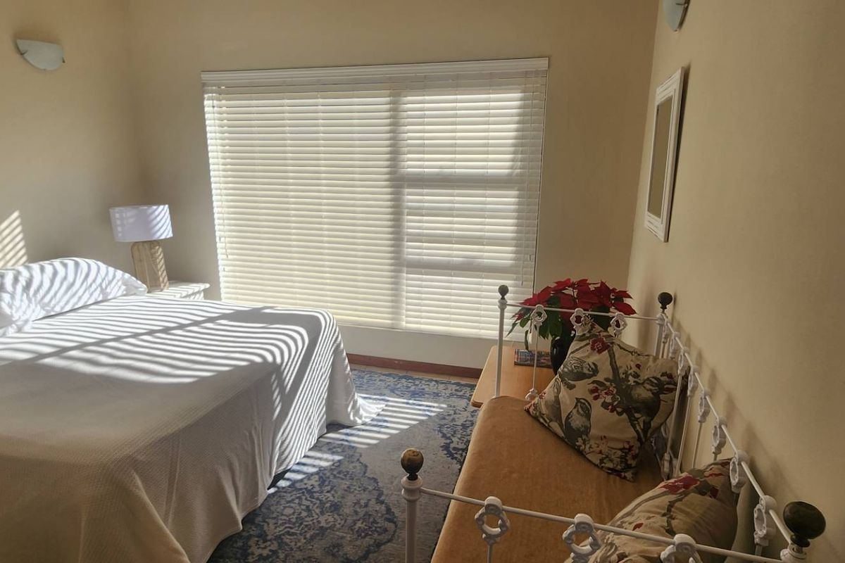 A well-lit bedroom featuring horizontal window blinds, neutral wall finishes, and wall-mounted lighting fixtures.