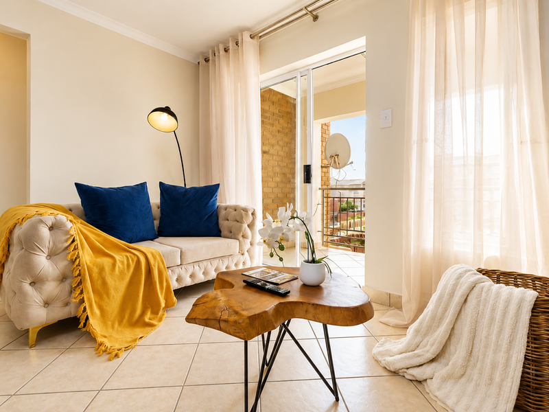 A bright living room featuring tiled flooring and a sliding glass door providing direct access to an outdoor balcony.