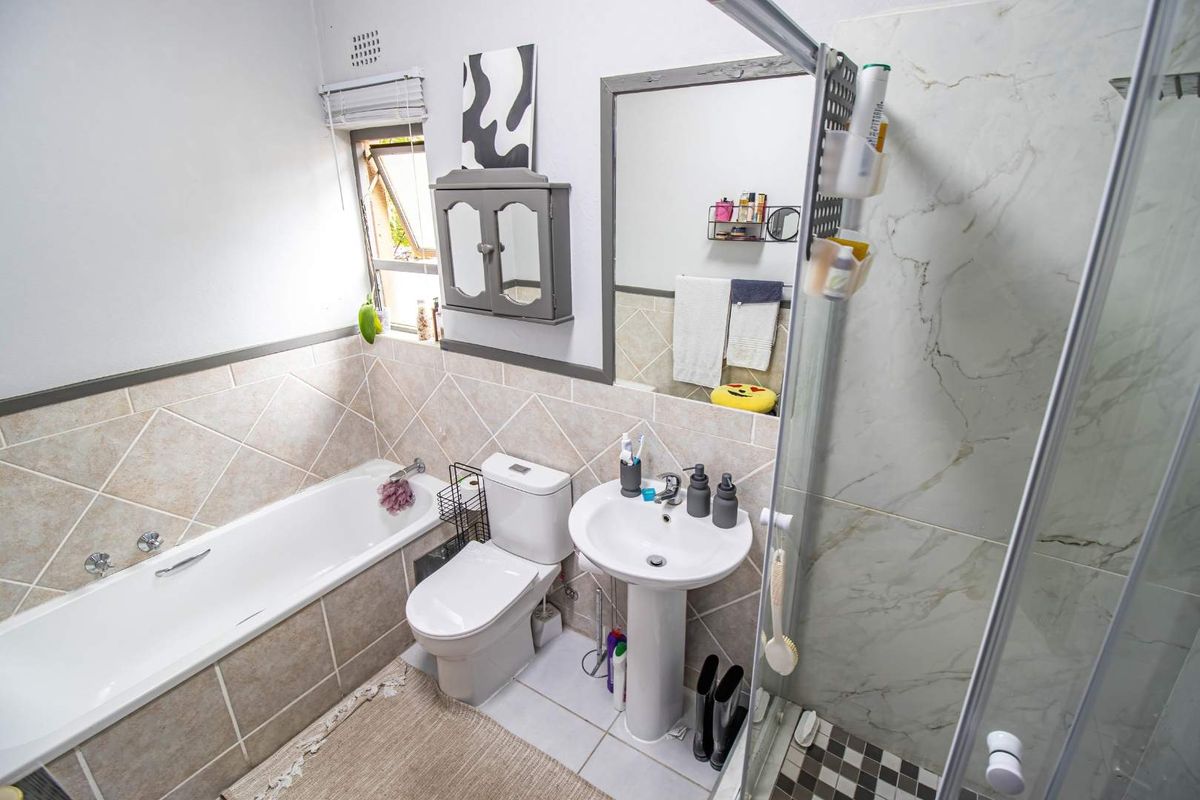 A well-maintained bathroom featuring a pedestal basin, a bathtub with tiled surround, and a separate glass-enclosed shower with marble-look wall tiles.