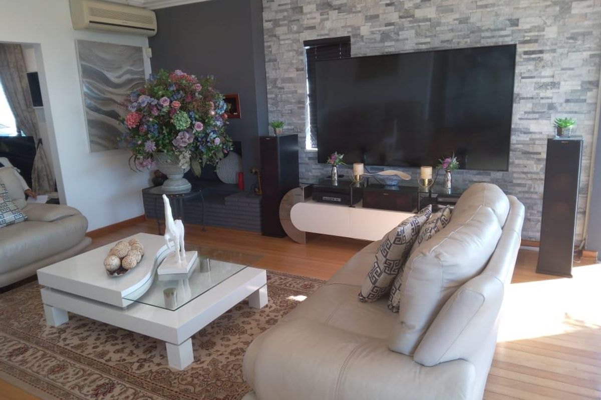 A well-maintained living room featuring a textured stone feature wall, timber flooring, and a wall-mounted air conditioning unit.