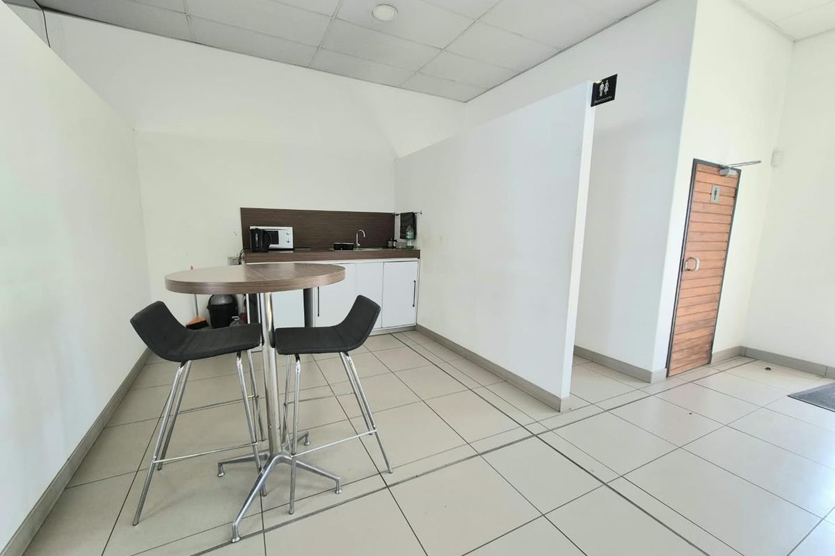 A functional office kitchenette area featuring compact cabinetry, a sink, tiled flooring, and direct access to a restroom facility.