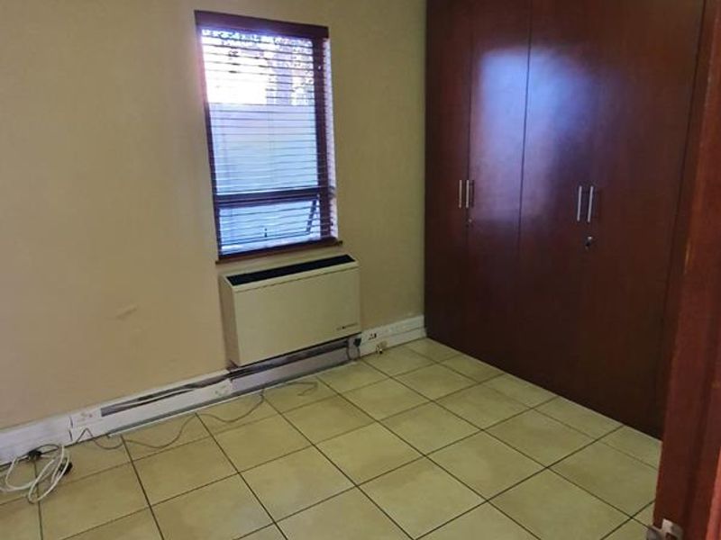 A functional bedroom featuring tiled flooring, built-in wooden cupboards, and an integrated HVAC unit, offering a clean and versatile space.