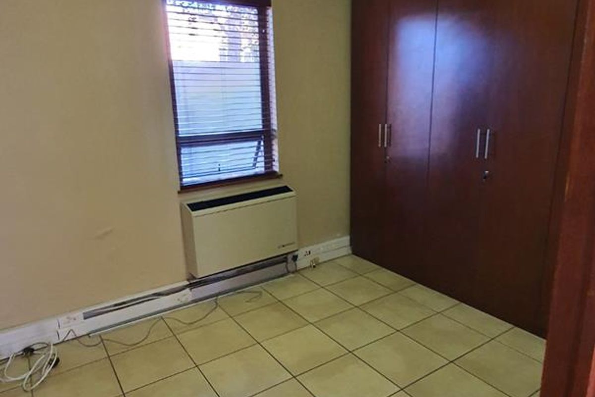 A functional bedroom featuring tiled flooring, built-in wooden cupboards, and an integrated HVAC unit, offering a clean and versatile space.