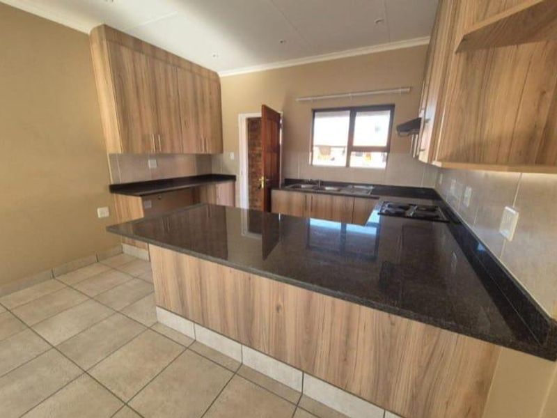 A modern kitchen featuring wood-finish cabinetry, dark granite countertops, a built-in hob, and tiled flooring in a clean, open-plan layout.