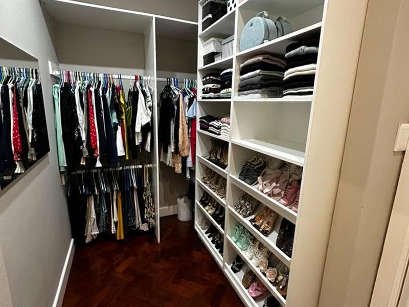 A walk-in closet featuring extensive built-in shelving, hanging rails, and classic parquet flooring.