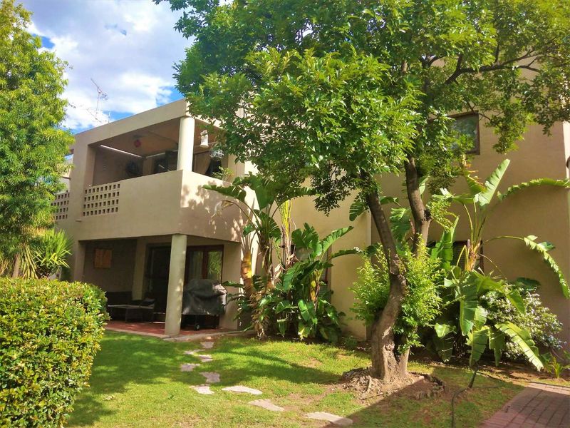 Rear view of the townhouse featuring a covered ground-floor patio, an upper-level balcony with decorative screening, and a mature landscaped garden.