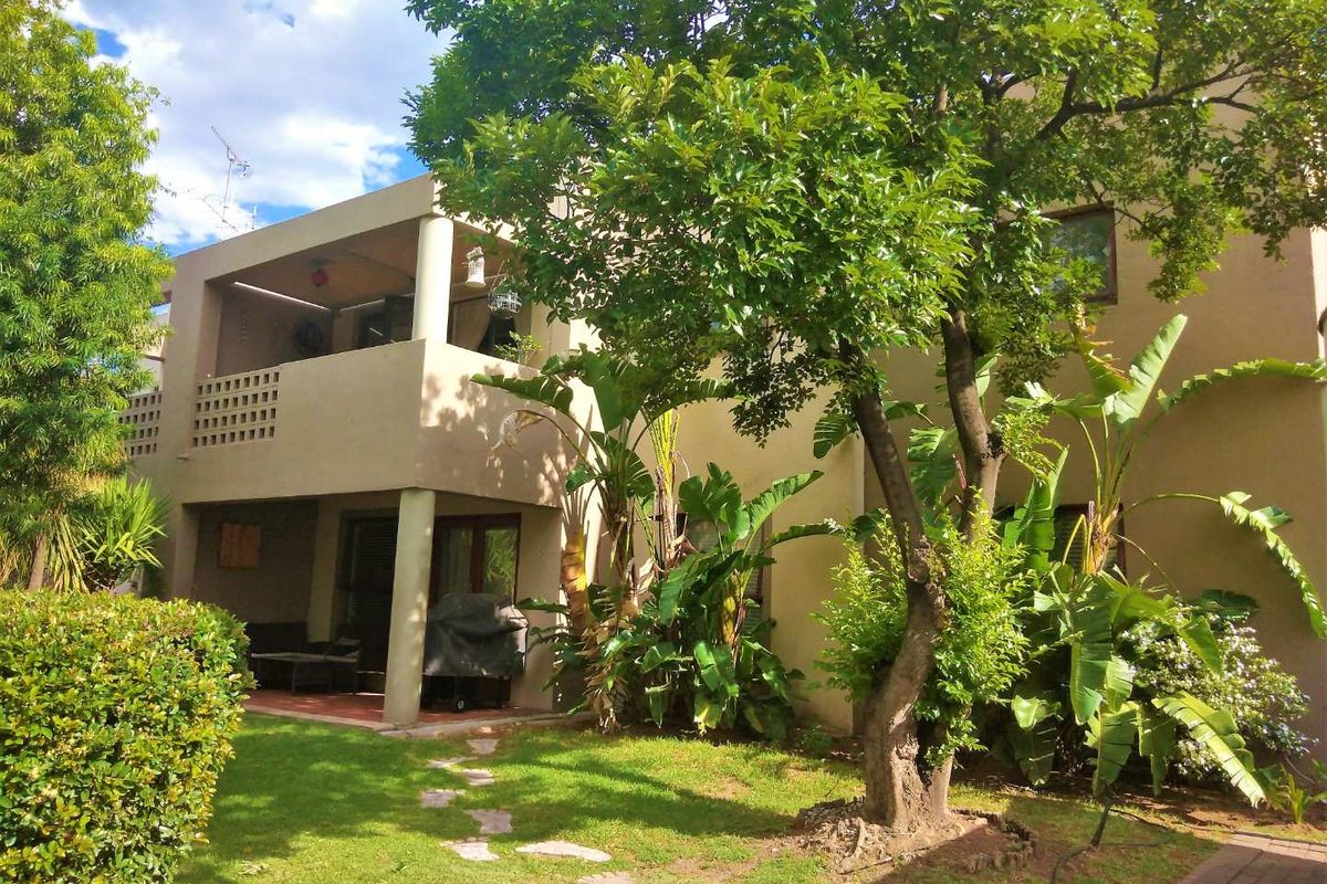 Rear view of the townhouse featuring a covered ground-floor patio, an upper-level balcony with decorative screening, and a mature landscaped garden.